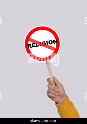 Atheism concept. Man holding prohibition sign with crossed out word Religion on light grey background Stock Photo