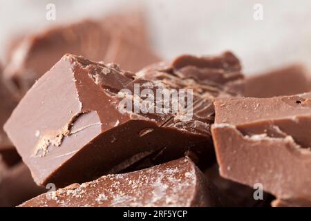 pieces of bitter chocolate are randomly scattered on the table, broken and crumbled natural bitter chocolate, edible bitter chocolate made from cocoa Stock Photo