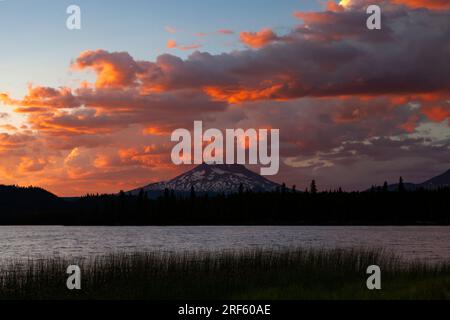 The skies glow at sunset above the Mount Bachelor volcano as it rises above Lava Lake in the Cascades Lakes area near Bend, Oregon. Stock Photo