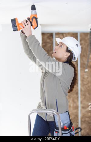 female builder using cordless drill on the ceiling Stock Photo