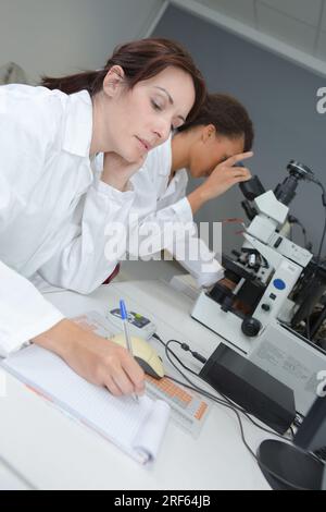 scientists working with microscope and taking notes in laboratory Stock Photo