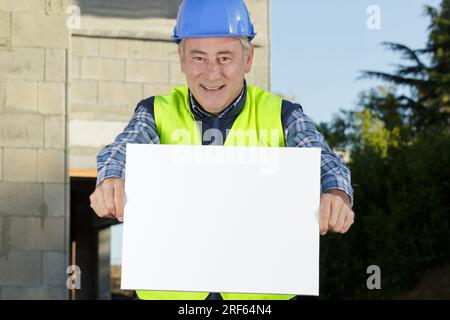 middle-age builder man pointing with finger at white blank banner Stock Photo