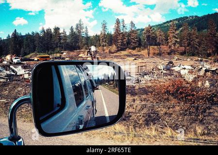 View from a moving vehicle through the passenger side window with a side view mirror or rear view mirror overlooking the old rusty metal, junkyard  in Stock Photo
