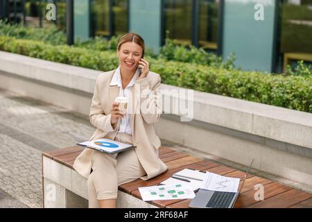 Smiling woman manager talking with client while working with documents outside of office  Stock Photo