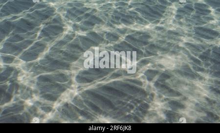 Glare of sun plays on sandy bottom in shallow water. Top view on sandy seabed in shallow water with diagonal lines of sand and sun glare on its surfac Stock Photo
