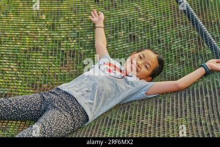 Happy time with Asian child girl lay down on wire bed or net bed in a resort, view from above, blank space for copy and design. Stock Photo