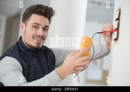 electrician checking the voltage level in wall socket cables Stock Photo