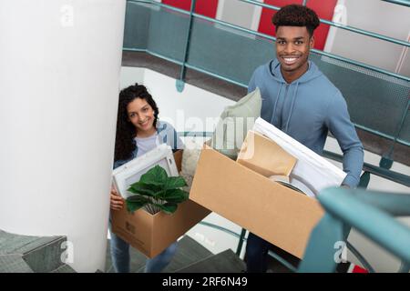 attractive multiracial couple carrying boxes on the stairs Stock Photo