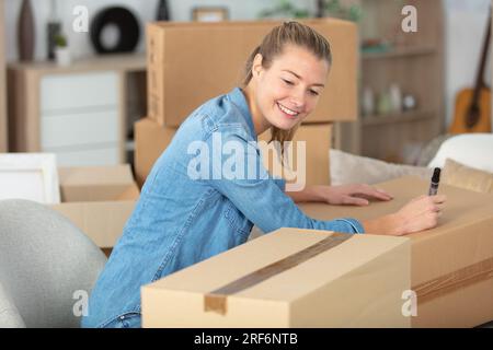 woman writing on boxes and smiling preparing to move house Stock Photo