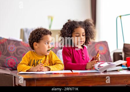 Two american kids sitting at home drawing writing reading, siblings having fun at home, homeschooling educational concept, brother and sister love Stock Photo