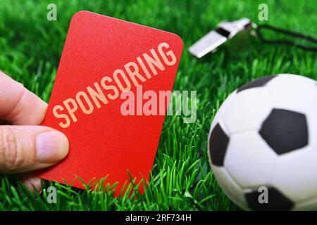 FOTOMONTAGE, Hand hält rote Karte mit Aufschrift Sponsoring auf Fußballrasen, Symbolfoto Kündigung von Sponsoring-Verträgen Stock Photo