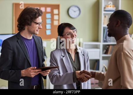 Portrait of young business people shaking hands with colleague in office and greeting each other smiling Stock Photo