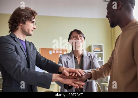 Side view at diverse business team of three people joining hands in unity celebrating success at office Stock Photo