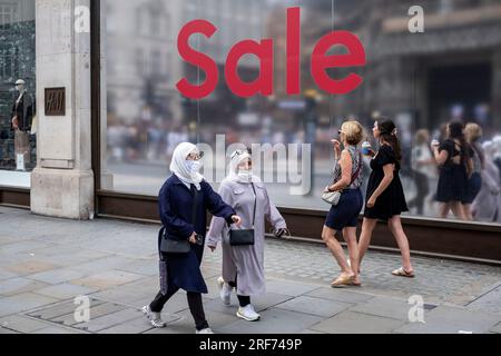 People out shopping walk past a large scale sale sign in red and silver for major high street clothing brand H&M outside their flagship store on the corner of Oxford Street and Regent Street on 9th July 2023 in London, United Kingdom. Oxford Street is a major retail centre in the West End of the capital and is Europes busiest shopping street with around half a million daily visitors to its approximately 300 shops, the majority of which are fashion and high street clothing stores. Stock Photo