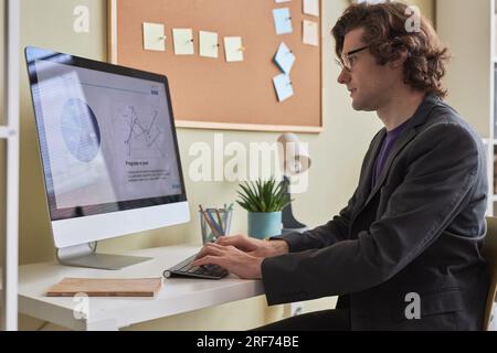 Side view portrait of smiling long haired man using computer at desk in office or at home workplace Stock Photo