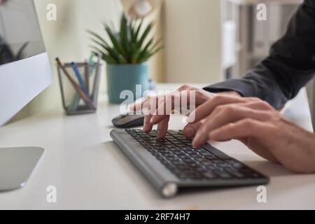 Closeup of male hands typing on wireless keyboard while using computer at office workplace, copy space Stock Photo