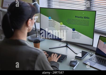 Back view at young woman using computer at desk while working on development strategies Stock Photo