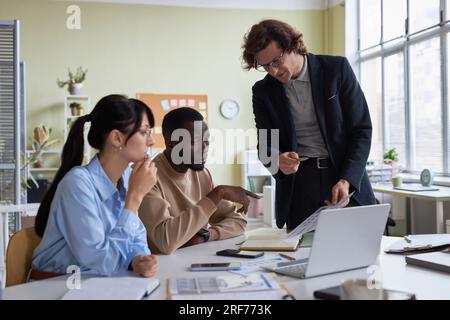 Diverse young business team of three people collaborating on project in office and discussing data Stock Photo
