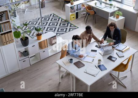 Wide angle top view of business team working together at meeting table in office and pointing at documents with data charts, copy space Stock Photo