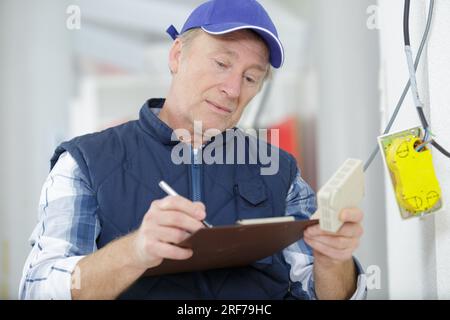 electrician looking at fuse box holding clipboard Stock Photo