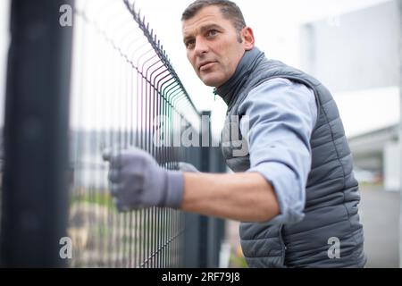 worker installing welded metal mesh fence Stock Photo