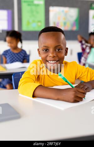 Happy biracial schoolboy sitting at desk and lying on books in ...