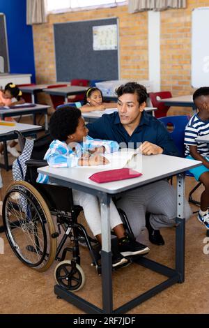 Biracial male teacher with boy in wheelchair in class at elementary school Stock Photo