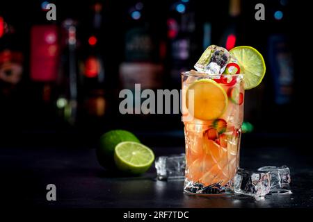Siam sunrays alcoholic cocktail drink with vodka, coconut liqueur, ginger, chili pepper, soda, lime juice, dark background, bar tools and bottles Stock Photo