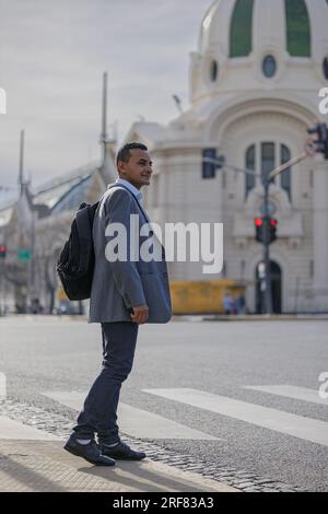 Latino man in a suit and backpack crossing the street in a city. Stock Photo