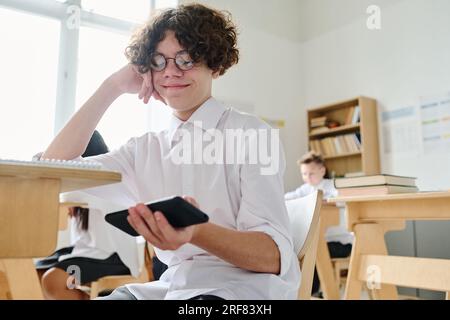 Student sitting at desk and using smartphone during lesson at school Stock Photo