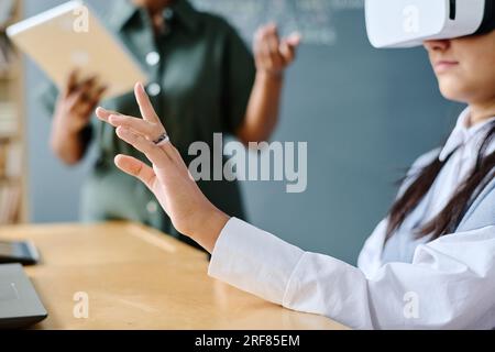 Student using VR glasses at lesson with teacher explaining information in background Stock Photo
