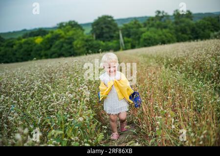 flag of Ukraine in hands of smiling little girl. happy child carries yellow-blue flag. day of Ukraine's insability. Stock Photo