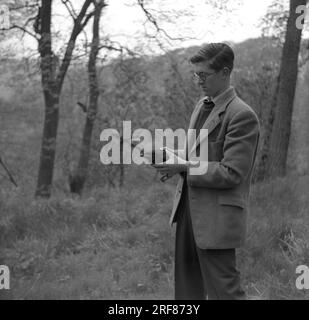 1950s, historical, a man in a sports jacket in a woody hillside standing holding a blackbird, possibly injured, England, UK. Stock Photo