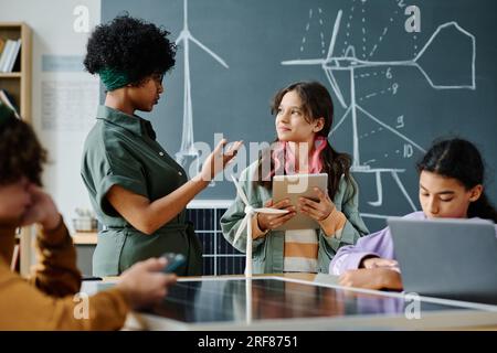 African American teacher talking to students at lesson while they using gadgets Stock Photo