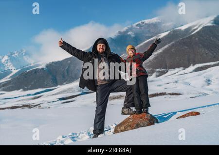Happy father and child waving hands and standing on mountains background at winter season Stock Photo