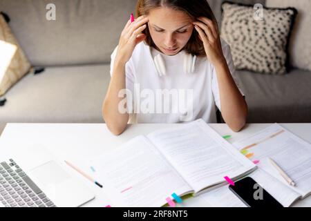 Student young brunette woman doing homework, thinking about exercise in her educational student's book, sitting at the desk and studying. Stock Photo
