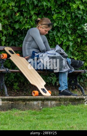young woman sitting on a bench with a skateboard. Stock Photo