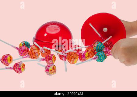 Close-up view of man's hands holding big plastic chupa chups package for several caramels isolated on pink  background. Stock Photo