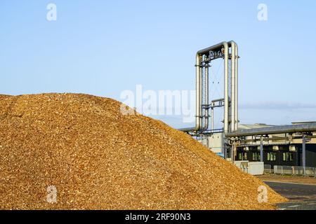 Exterior view of a modern biomass cogeneration wood chip power plant facility equipment with a mountain of wood chips in the foreground Stock Photo