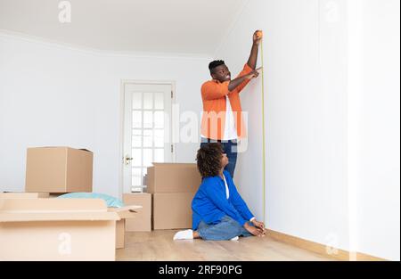 Black Man And Woman Making Repair After Moving, Using Tape Ruler Together Stock Photo