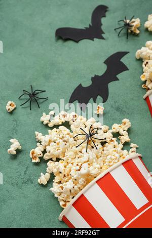 Bucket with tasty popcorn, spiders and paper bats on green background, closeup. Halloween celebration Stock Photo