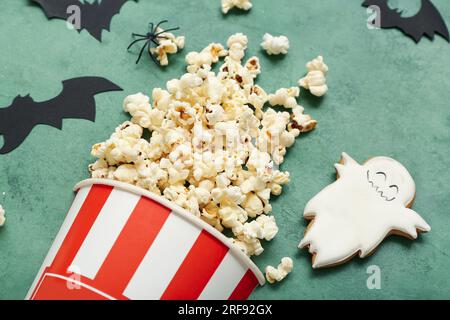 Bucket with tasty popcorn, cookie and paper bats on green background, closeup. Halloween celebration Stock Photo