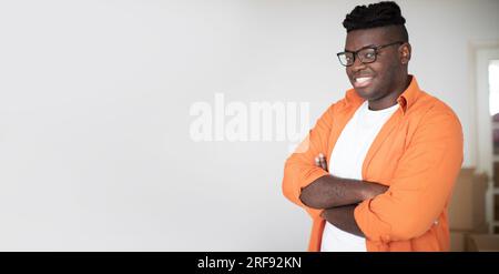 Smiling Young African American Man Posing With Folded Arms Against Cardboard Boxes Stock Photo