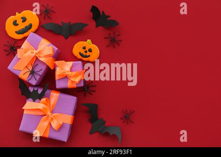 Composition with spiders, bats, gift boxes and tasty cookies for Halloween on burgundy background Stock Photo