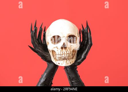 Black hands of witch with skull on red background. Halloween celebration Stock Photo