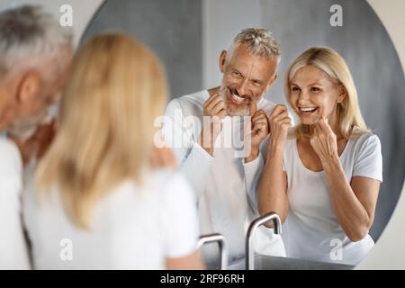 Morning Routine. Smiling Mature Couple Using Dental Floss In Bathroom Together Stock Photo