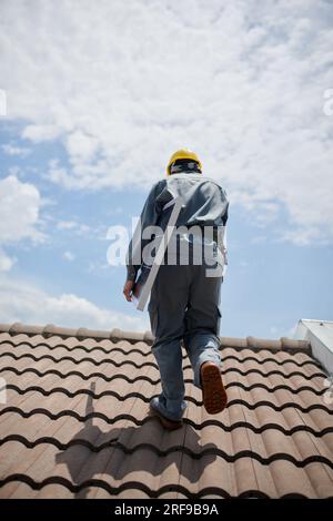 Engineer carrying solar panel when walking on roof, view from back Stock Photo