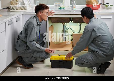 Plumbers fixing leaking sink in kitchen Stock Photo
