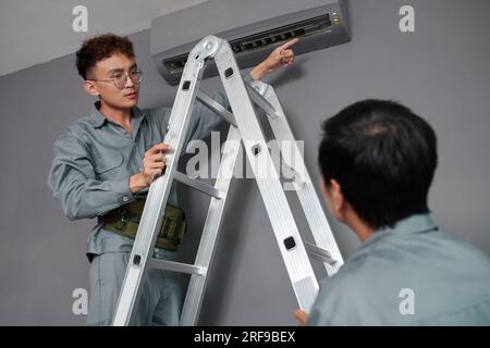Workers installing air conditioner on wall in house of client Stock Photo