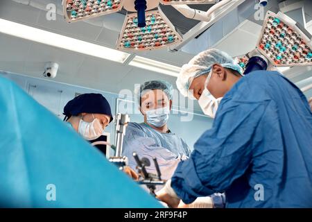 Low angle view of surgeons leaned over patient during complex surgical operation in a sterile operating room. Doctors are focused and extremely attent Stock Photo